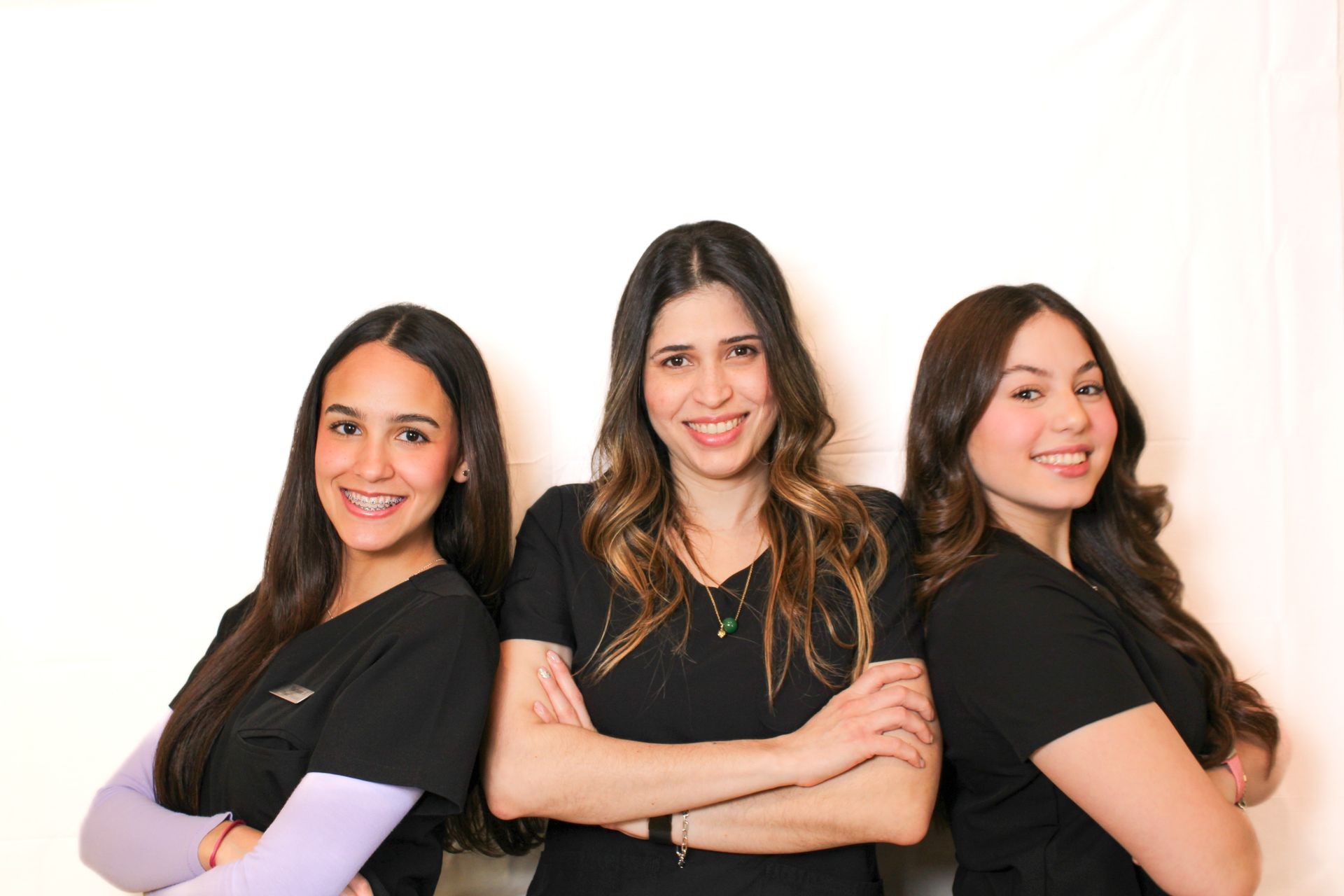 Three women in black outfits smiling confidently with arms crossed, standing against a plain white background.